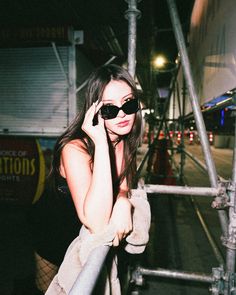 a woman in sunglasses is talking on her cell phone while standing next to a fence