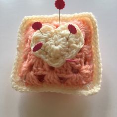 a small crocheted square with a heart on the top and two pins in the middle