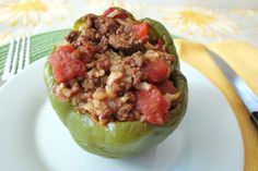 a green pepper stuffed with meat and vegetables on a white plate next to a fork