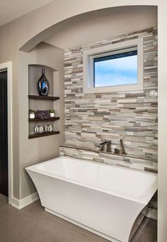 a white bath tub sitting under a window next to a wall mounted shelf filled with vases