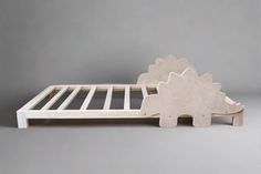 a wooden bed frame with a dinosaur design on the top and bottom, sitting in front of a gray background