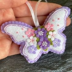 a hand holding a purple and white butterfly ornament with flowers on it's wings