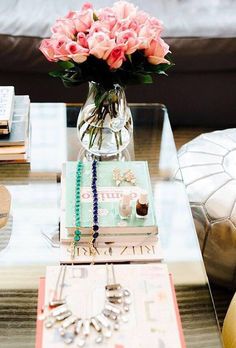 pink flowers in a vase sitting on top of a table next to books and jewelry