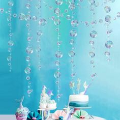 a table topped with cake and cupcakes covered in bubble wands next to a wall hanging from the ceiling