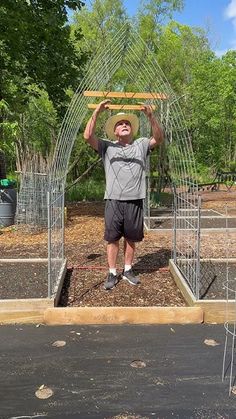 a man standing in the middle of a garden holding up a wooden frame over his head