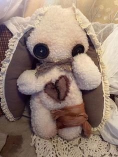 a white teddy bear sitting on top of a bed next to a lace doily