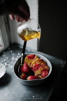 a person pouring syrup over a bowl of food on top of a stove with strawberries in it