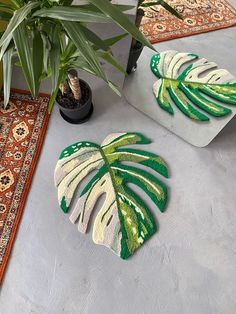 two green and white leaf shaped rugs sitting on top of a floor next to a potted plant