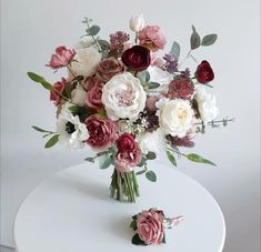 a bouquet of flowers sitting on top of a white table next to another flower arrangement