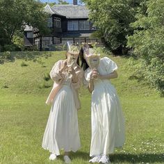 two women in white dresses are standing on the grass with their faces covered by masks