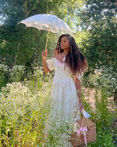 a woman in a white dress holding an umbrella while standing in tall grass and flowers