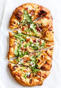 the pizza is cut into four slices and has many toppings on each slice, including arugula