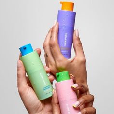 two hands holding three different types of hand sanitizers in front of a gray background