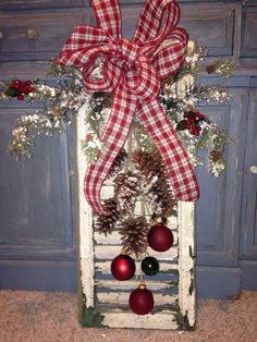 an old window decorated for christmas with pine cones, ornaments and a bow on it