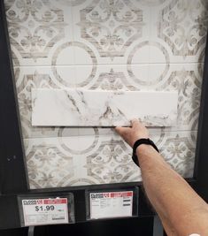 a man is pointing to the tile on the wall in front of him and another person's hand