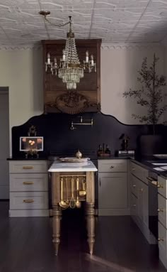 a kitchen with white cabinets and gold trimmings on the ceiling, chandelier above the sink