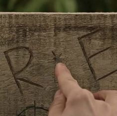 a person is pointing at the letters on a piece of wood