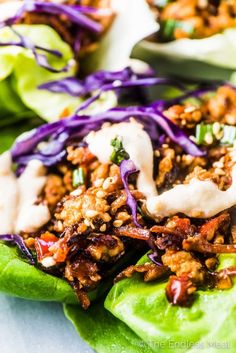 lettuce wraps filled with meat and vegetables on a white plate topped with dressing