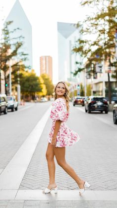 a woman is standing on the sidewalk in front of some cars and buildings with her legs crossed