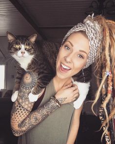 a woman holding a cat in her arms and smiling at the camera with dreadlocks on her head