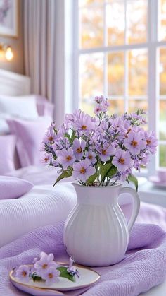 a white vase filled with purple flowers on top of a bed