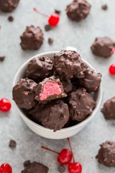 a white bowl filled with chocolate candy and cherries on the table next to it