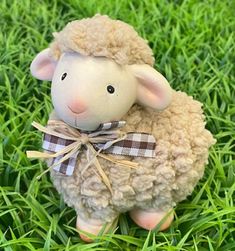 a toy sheep with a bow on its head sitting in the middle of some grass