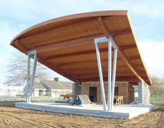 a large wooden covered structure sitting on top of a dirt field next to a building