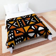 an orange and black comforter on a bed in a room with wood flooring