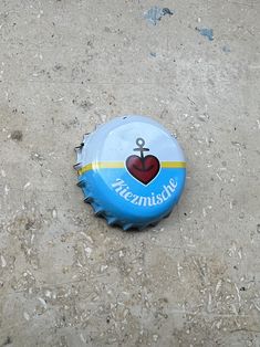 a blue bottle cap with a heart and anchor on it sitting on the ground in front of a building