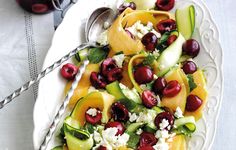 a white plate topped with fruit and cucumber salad next to a jar of cherries