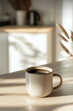 a coffee cup sitting on top of a wooden table next to a vase with dry grass in it