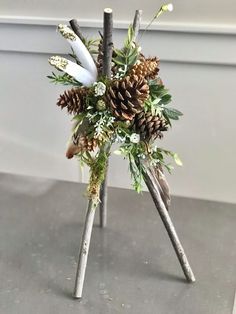 two sticks with pine cones and flowers in them on top of a table next to a wall