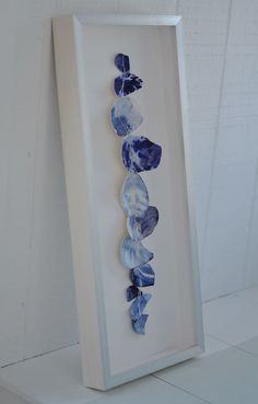 a white frame with blue flowers in it on a shelf next to a wall mounted art piece