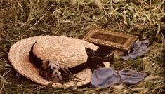 a straw hat and blue scarf laying on the grass next to an old photo frame