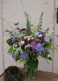 a vase filled with purple and white flowers on top of a wooden table next to a bird nest