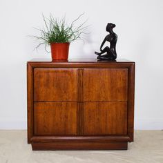 a wooden cabinet with a potted plant on top and a statue sitting on it