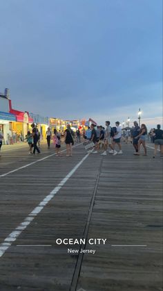 people are walking on the boardwalk at ocean city, new jersey as dusk falls in the background