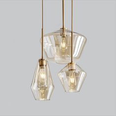 three clear glass pendant lights hanging from a ceiling fixture with gold fittings on the sides