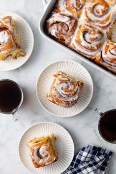 three plates with cinnamon rolls on them next to two cups of coffee