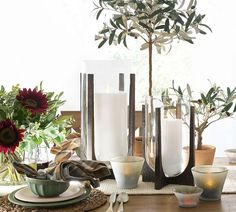 a table topped with vases filled with flowers next to candles and plates on top of a wooden table