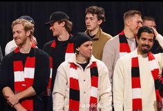 a group of men standing next to each other in front of a black background wearing red and white scarfs