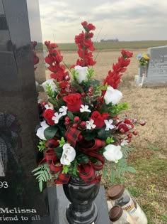 a vase filled with red and white flowers on top of a black table next to a grave