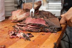 a person cutting up meat on top of a wooden table