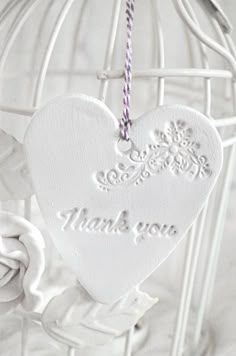 a white heart shaped ornament hanging from a birdcage with the words thank you written on it