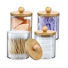 three glass containers with wooden lids and spoons next to each other on a white background