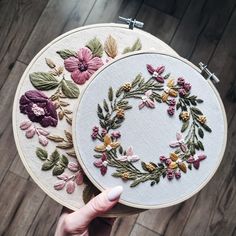 two embroidered hoops with flowers and leaves on them, one being held by a woman's hand