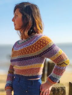 a woman standing next to a wooden fence near the ocean with her hands on her hips