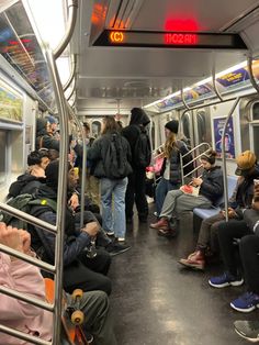 many people are sitting and standing on the subway car, all wearing winter coats or hats