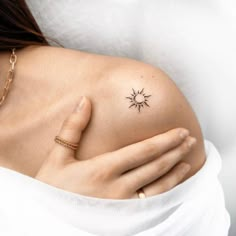 a woman's shoulder with a small tattoo on her left arm and the sun in the middle